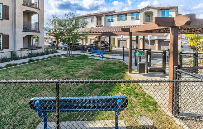 A blue bench sits in front of a fence in a grassy area.