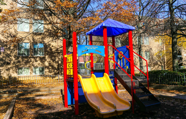 a playground with slides and a swing set in front of an apartment building