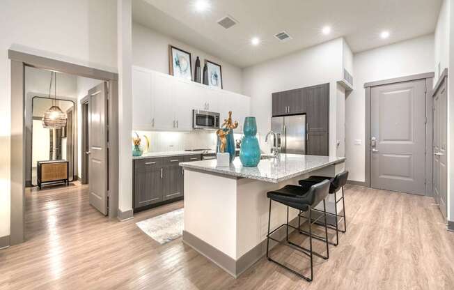 A kitchen with a white island and black bar stools.at The Bridge at McKinney, McKinney