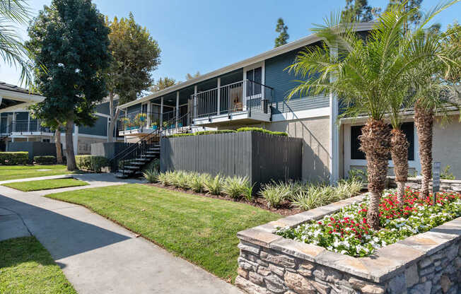 A building with a balcony and a stone planter with palm trees in front.