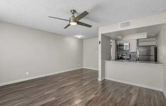 an empty living room with a ceiling fan and a kitchen