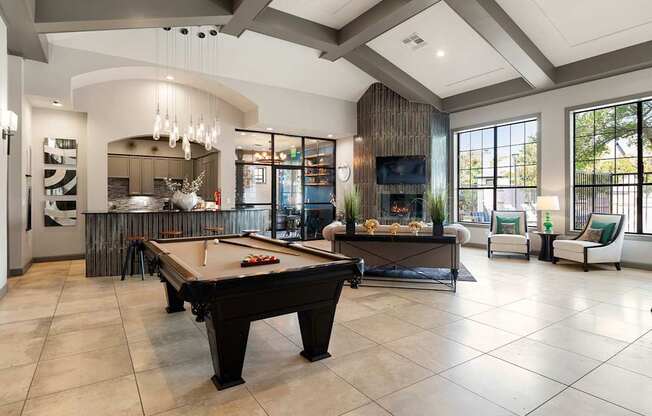 Clubhouse lounge with billiards table, seating area, large windows, and open kitchen bar.