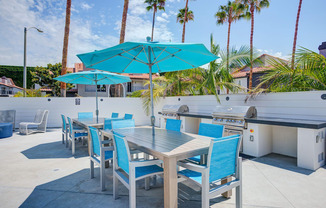 a patio with a grill and tables with blue chairs and umbrellas  at Laguna Gardens Apts., Laguna Niguel