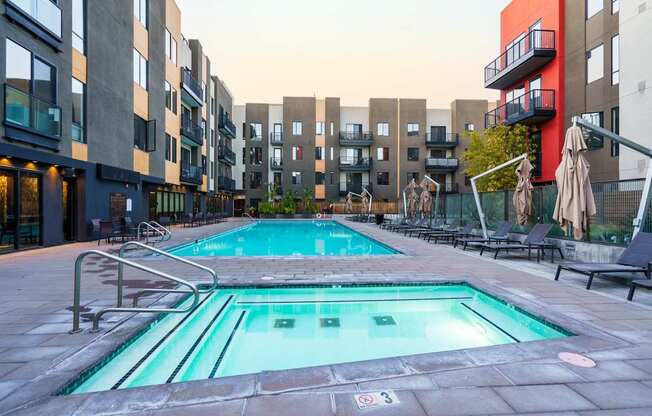A swimming pool surrounded by buildings and lounge chairs.