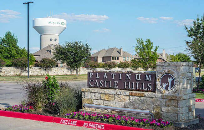 a stone sign with a water tower behind it in front of a parking lot