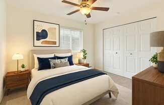 A bedroom with a bed, a ceiling fan, and a nightstand with a lamp.