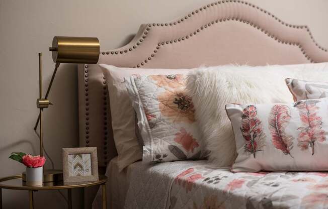 A bed with a pink headboard and floral pillows is shown.