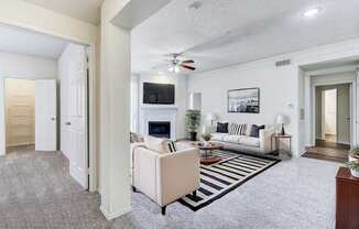 Spacious living room in Saxony at Chase Oaks Apartments in Dallas, TX, featuring a staged modern design with neutral-colored sofas, striped area rug, fireplace with a mounted TV, and large windows for natural light.
