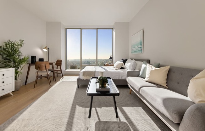 a living room with a couch and a table and a large window at The Paxton, Brooklyn, 11201