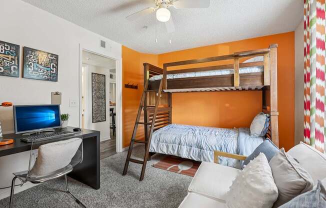 A room with a bunk bed, a desk with a computer, and a chair.