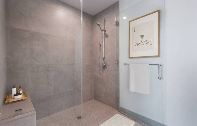 A bathroom with a glass shower stall and a towel rack with a heart-shaped picture hanging on the wall.