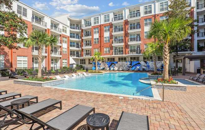 A courtyard pool surrounded by palm trees and lounge chairs at The Grand At Upper Kirby in Houston, TX