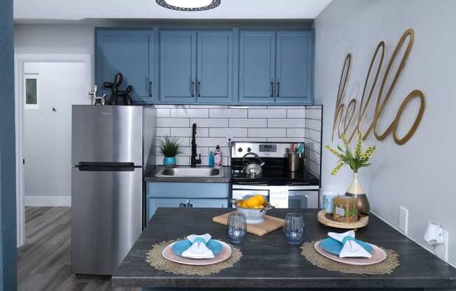 Fusion Las Vegas apartment kitchen with stainless steel appliances, navy blue cabinets, subway tile backsplash, and two place settings on island.