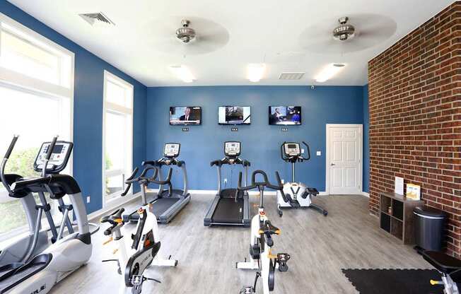 A gym with a variety of cardio equipment and a brick wall.