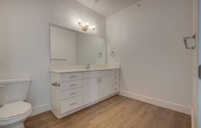 A white bathroom with a toilet, sink, and wood flooring.