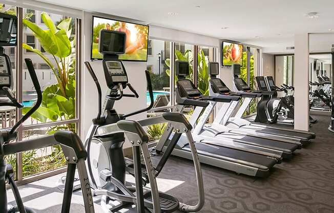 Apartments for Rent in Redwood City, CA - mResidences Redwood City - Fitness Center with Large Windows, View of the Pool, Equipment, TV, and Carpeted Floor