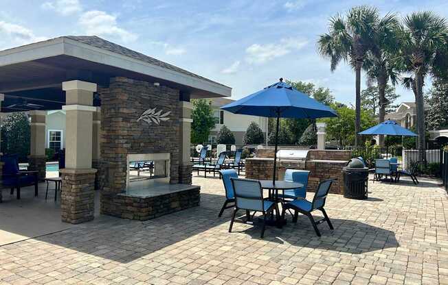 A patio with a fireplace and chairs under a blue umbrella.