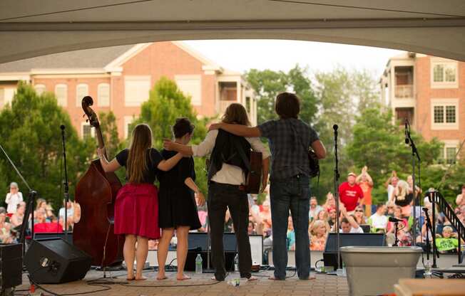 A concert at Eagleview Town Center showing the backside of four performers with their instruments on an outdoor covered stage with a crowd of people watching them.