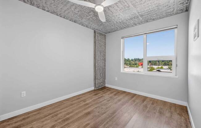 A room with a ceiling fan and a window overlooking a residential area.