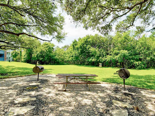 A picnic table is set up in a gravel area with trees in the background.