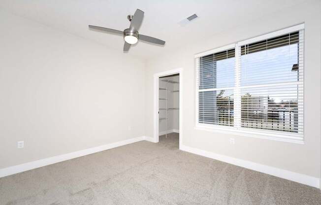 A room with a fan and a window with blinds.