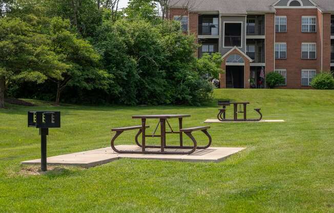 two picnic tables in a park in front of an apartment building