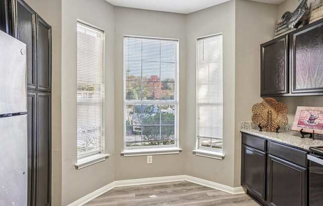 A kitchen with a refrigerator, cabinets, and a window with blinds.