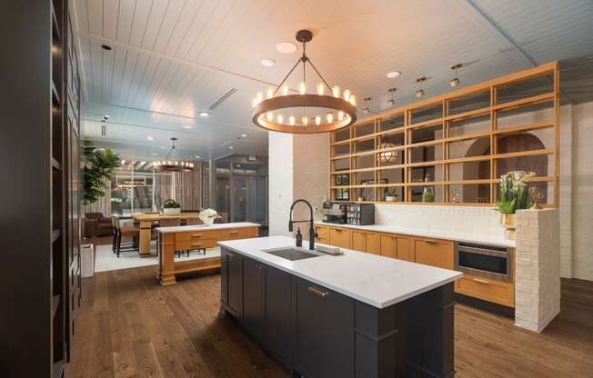 Gorgeous resident kitchen and lounge area with a patterned wood and brick half-wall, dark island cabinetry with gold hardware and sink, and view into the chic seating area at Sylvan Uptown, Denver, CO