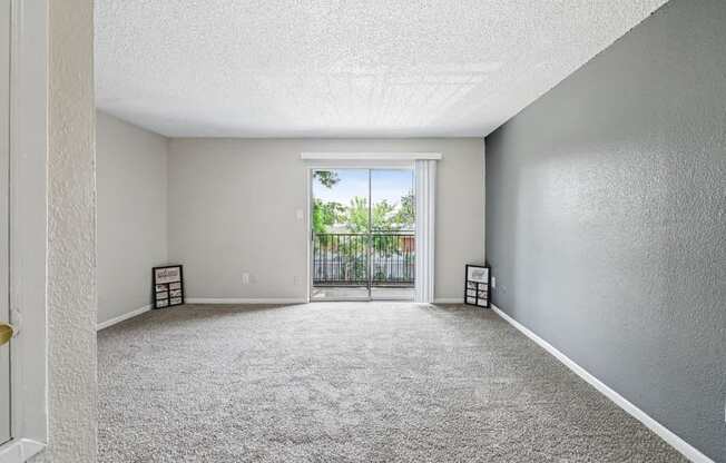A room with a carpeted floor and a sliding glass door leading to a balcony.
