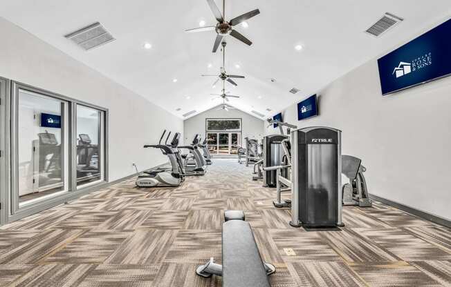 a gym with cardio machines and a ceiling fan