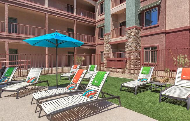Poolside chaise lounge chairs placed around sparkling blue pool in front of apartment buildings