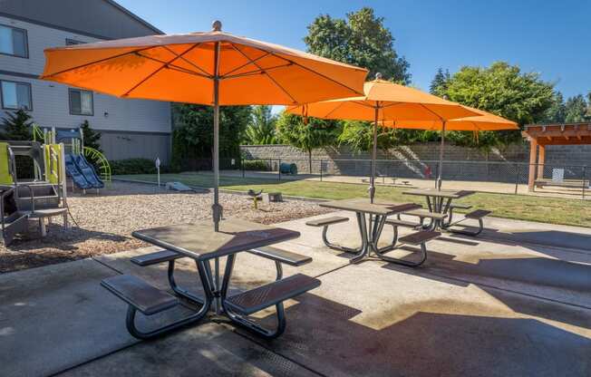 two orange umbrellas and picnic tables in a park