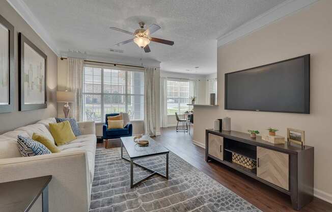 A living room with a white couch, a coffee table, and a flat screen TV mounted on the wall.