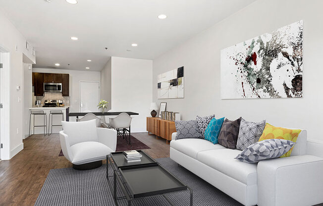 Hardwood floored living room with can lights and view of kitchen.