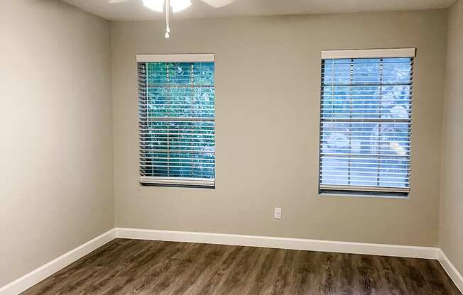 an empty bedroom with two windows with wood flooring