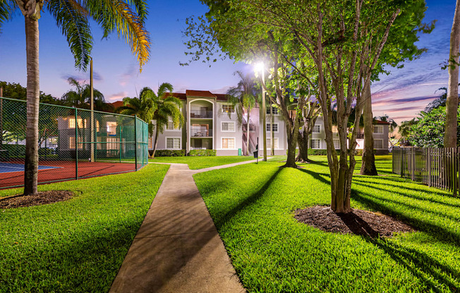 A pathway leads through a grassy area with trees and a tennis court.