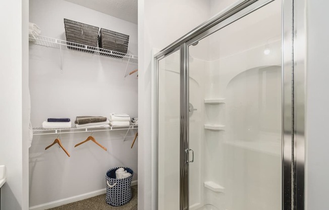 A bathroom with a white shower stall and a white towel rack with towels hanging on it.