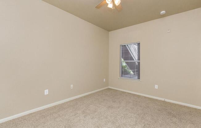 Bedroom with tan carpet, ceiling fan, and window with blinds