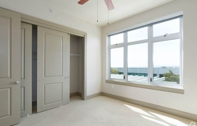 A room with a window overlooking the city and a ceiling fan.