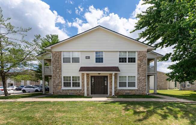the front of a white house with a lawn and trees