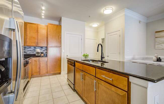 Apartments Near National Harbor - Tribeca at Camp Springs - A kitchen with wooden cabinets and a black countertop
