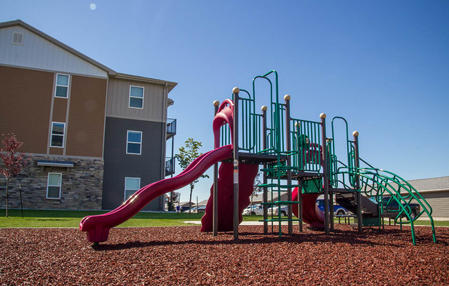 a playground with a slide and climbing equipment in front of an apartment building