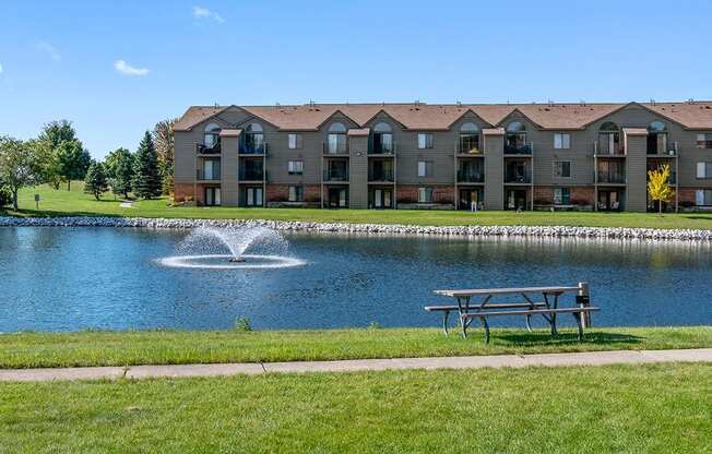 An exterior building with a pond, fountain and picnic table at Oak Shores Apartments in Oak Creek, WI
