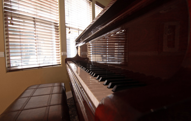 A brown piano sits in front of a window with blinds.,A brown piano sits in front of a window with blinds.