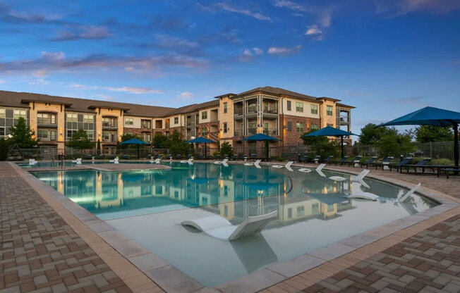 A large swimming pool in front of a building with a sunset sky.
