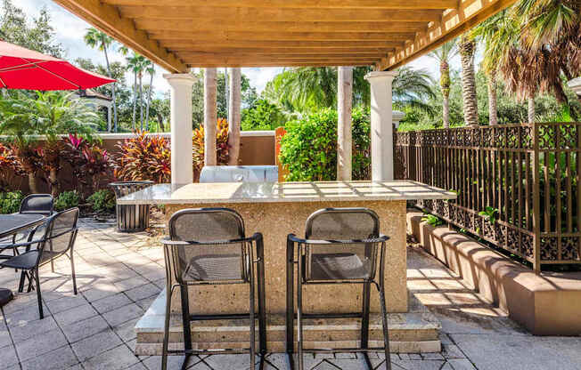 Outdoor grilling station under a pergola with bar seating and tropical landscaping