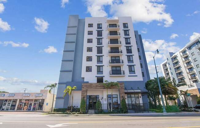 A modern multi-story building with a flat roof and a parking lot in front.