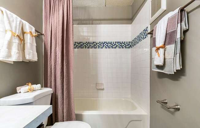 A bathroom with a white tub, a pink shower curtain, and a white towel hanging on the towel rack.
