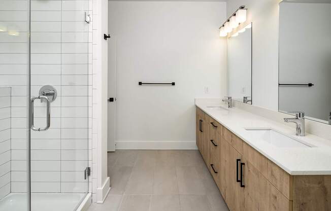 A white tiled bathroom with a walk-in shower and double sink vanity.