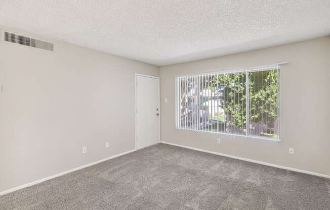 an empty living room with a large window and carpeting